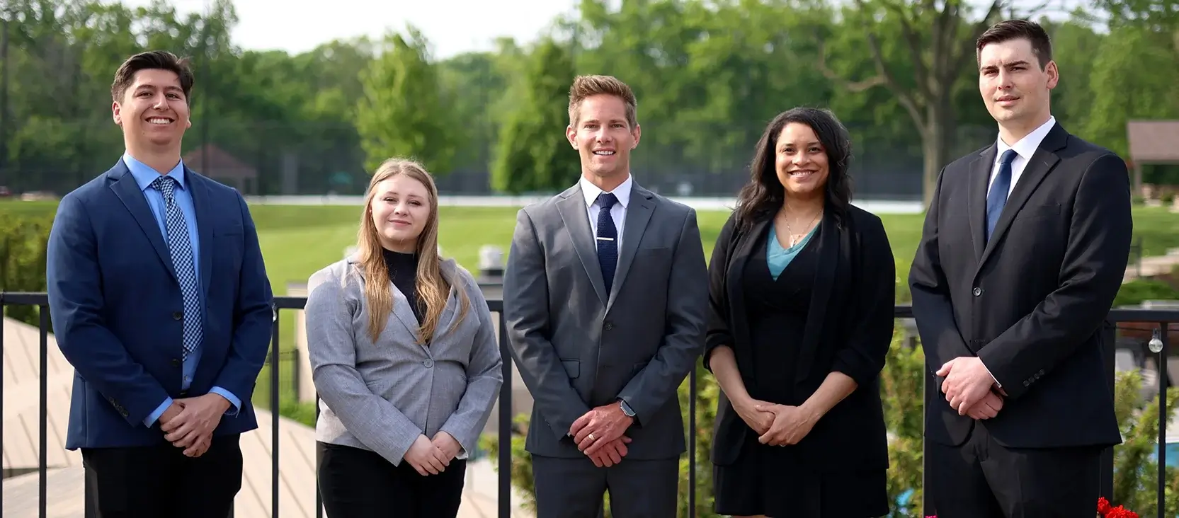 A group of five young individuals dressed in business attire, standing closely together in a professional setting.