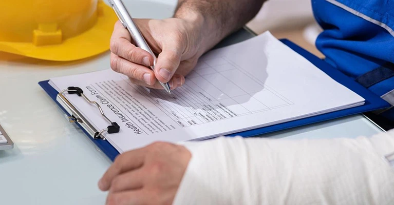 Injured construction worker filling out health insurance claim form with a broken arm.