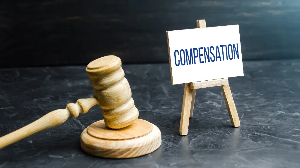 Wooden judge's gavel resting beside a small easel with the word "COMPENSATION" displayed.