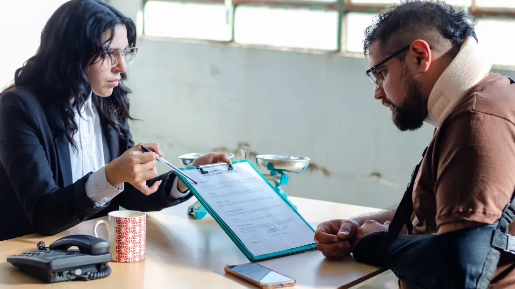 Professional woman explaining a document to an injured man with arm sling and neck brace.