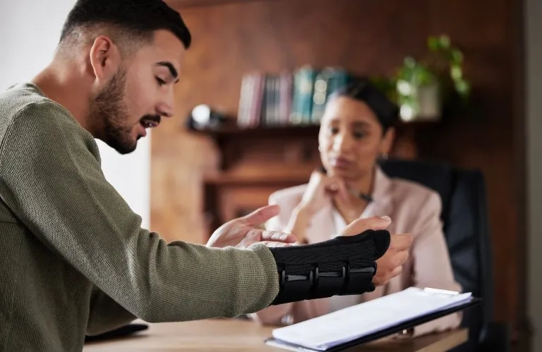 Man with a wrist brace explaining injury to a female professional in an office setting.